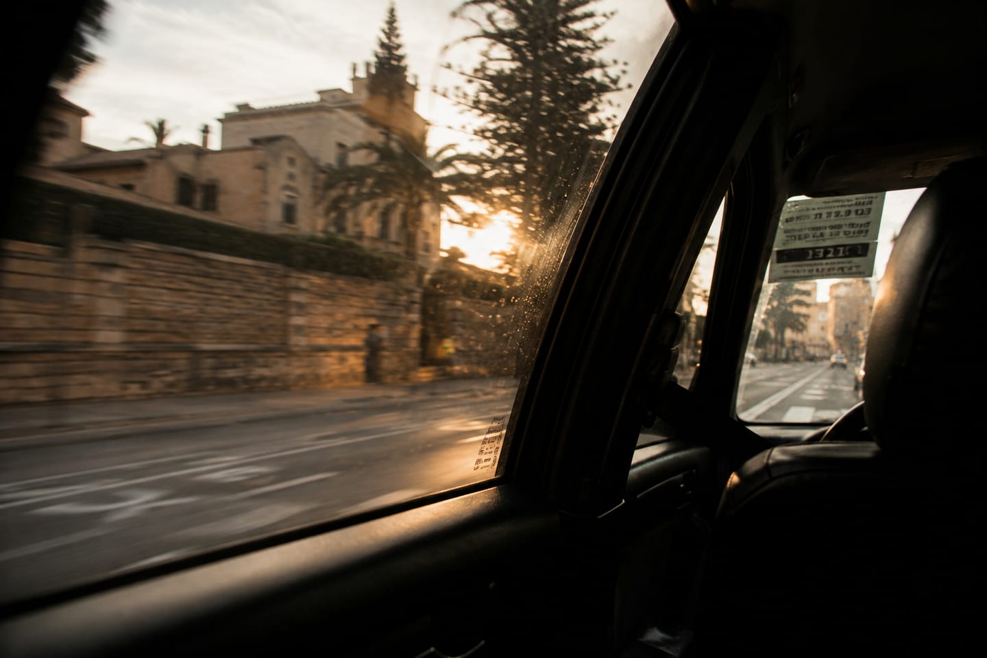 View from the back of a taxi in Palma de Mallorca — golden hour catching a stone wall, palms and a finca with the cathedral barely visible beyond.