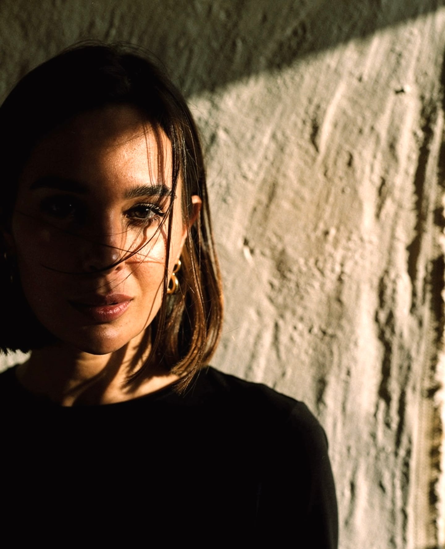Editorial character-study portrait of Nathaly Fernandez against a plaster wall in Palma de Mallorca, afternoon light catching half the face, hair caught by movement.